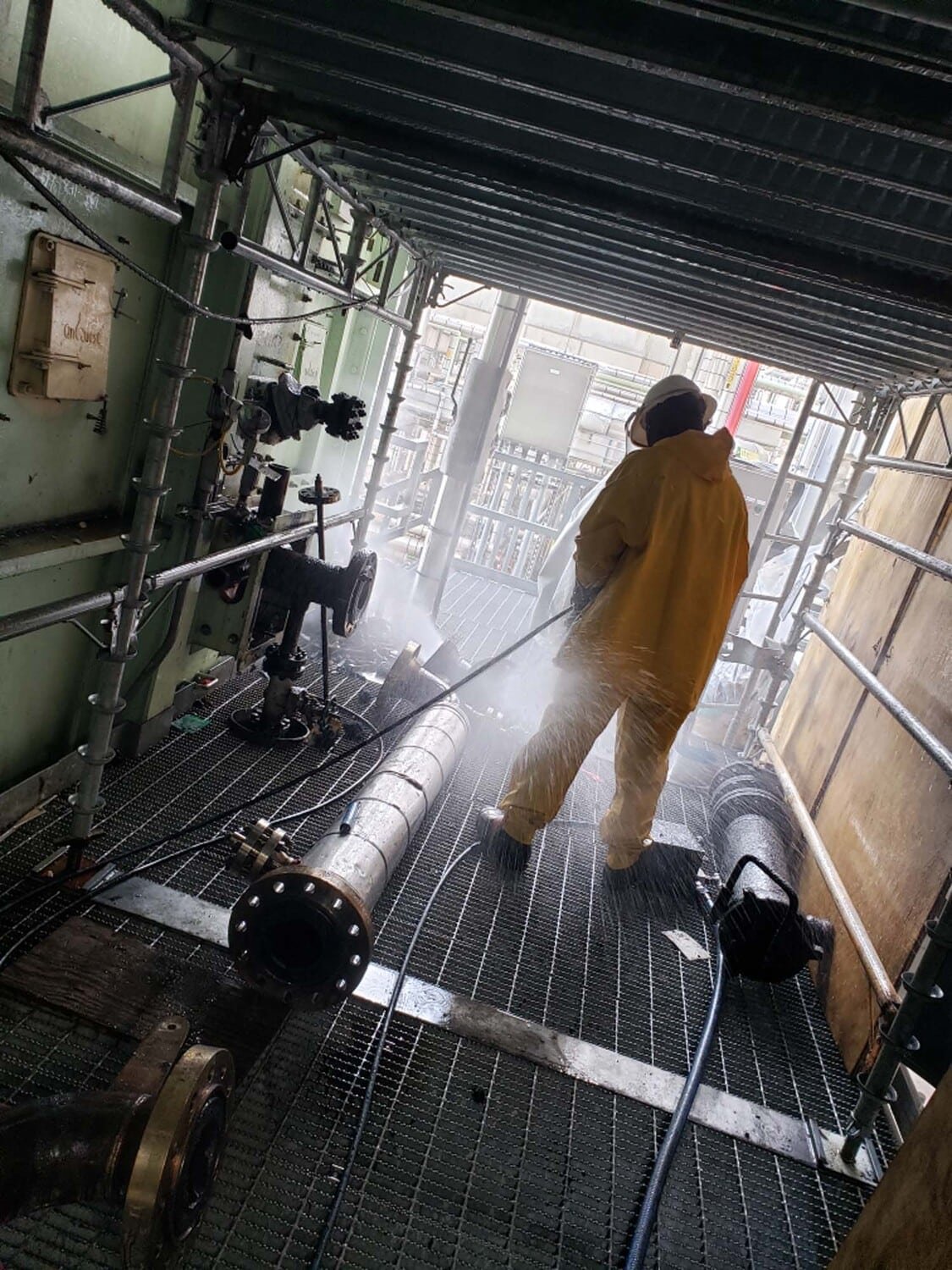 Industrial worker power-washing grated flooring area